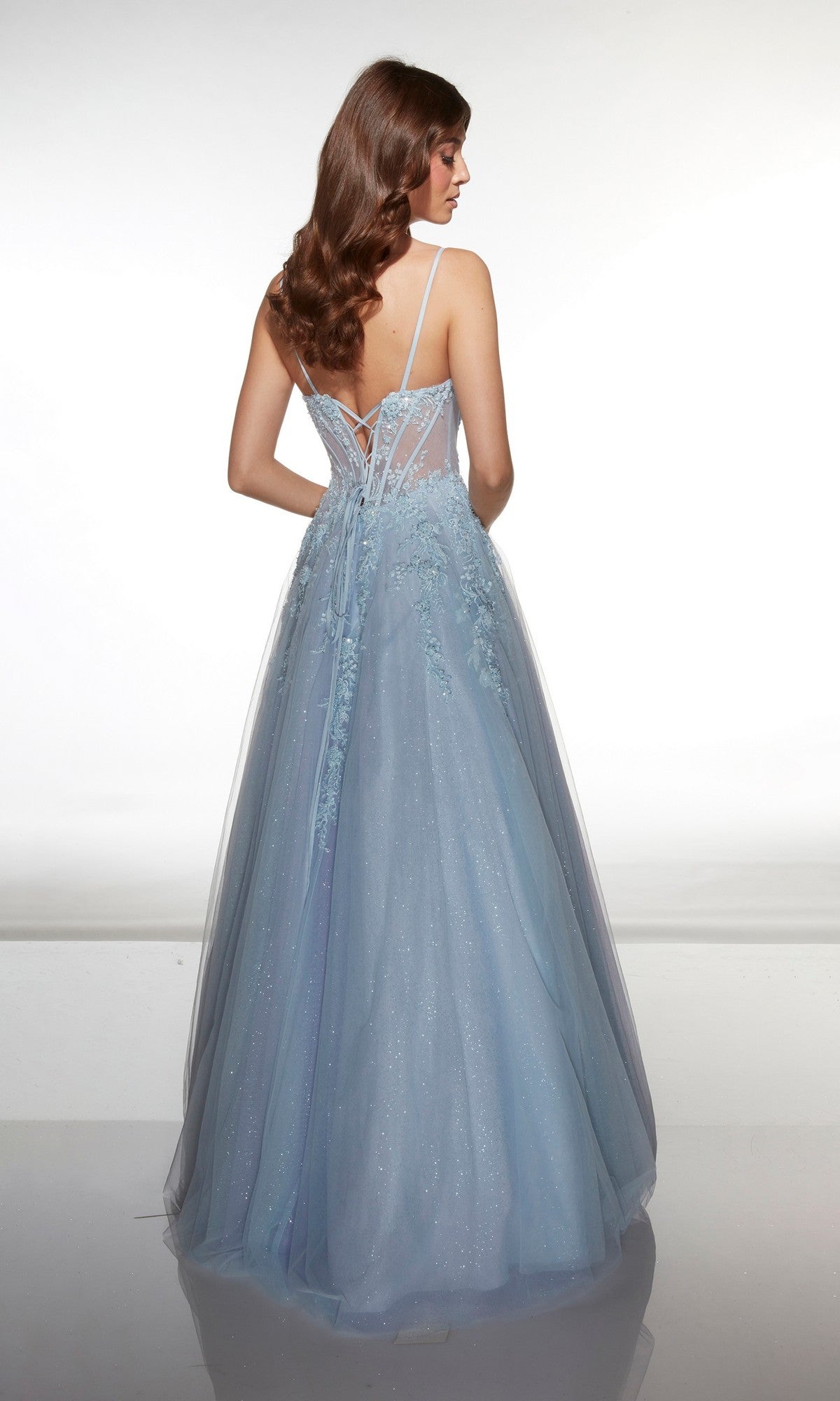 A woman models the Alyce 62061 long prom dress, a light blue sleeveless gown with a lace corset bodice, thin straps, sheer lace-detailed back, and flowing floor-length skirt against a plain white background.